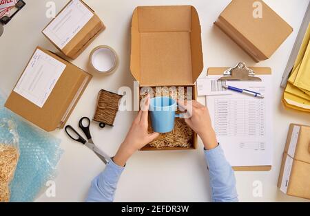 consegna la tazza di imballaggio alla scatola del pacco presso l'ufficio postale Foto Stock