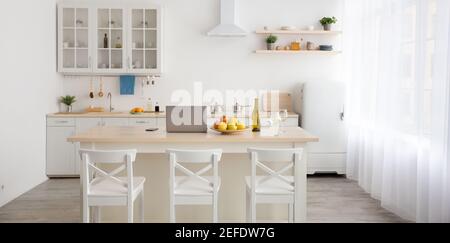 Interno minimalista sala da pranzo e cucina elegante, affitto, annuncio e vendita di appartamento. Mele, computer portatile e telefono, bicchieri e bottiglia di vino da tavola, sedie, Foto Stock