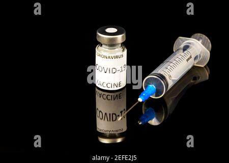 Etichetta di vaccino in flaconcino di vetro Covid - 19 testo del vaccino Coronavirus e siringa medica isolata in nero Foto Stock
