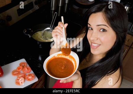 Ritratto di una giovane donna che tiene una ciotola di pomodoro zuppa in cucina Foto Stock