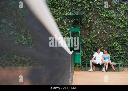 Un uomo medio adulto e una giovane donna seduta su un panca su un campo da tennis Foto Stock