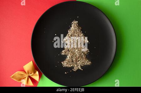 Albero di Natale fatto di sabbia su un piatto nero su uno sfondo colorato Foto Stock