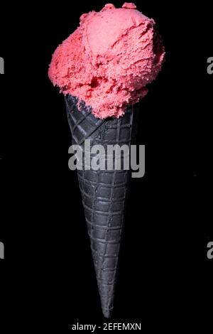una palla di gelato alla fragola in un ghiaccio nero cialda di crema isolata su sfondo nero Foto Stock