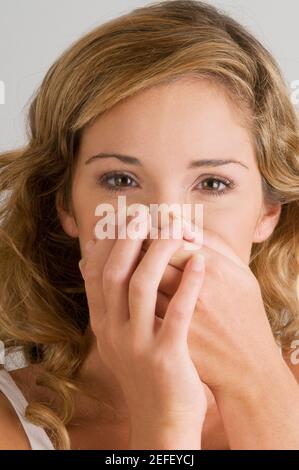 Ritratto di una giovane donna che copre la bocca con le mani Foto Stock