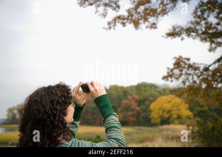 Vista posteriore di una donna di mezza età che fotografa con un fotocamera digitale Foto Stock