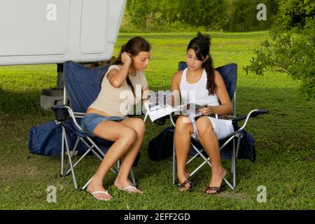 Due ragazze adolescenti sedute in poltrone e leggendo una rivista Foto Stock