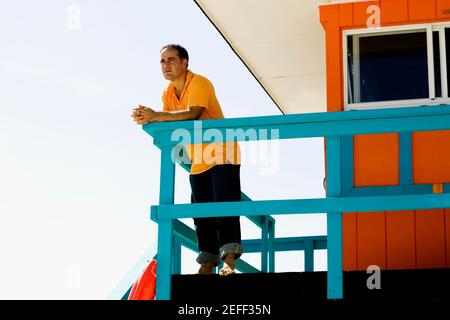 Vista ad angolo basso di un uomo medio adulto appoggiato una ringhiera di una capanna di bagnino Foto Stock