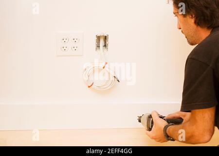 Vista posteriore di un uomo medio adulto che tiene una mano trapano Foto Stock