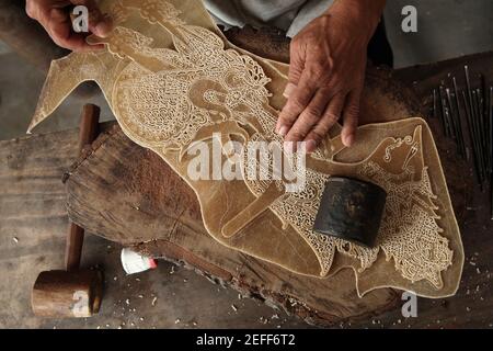 Artigiano fa un burattino di pelle di Rama per il teatro wayang kulit nel negozio di artigianato classico Wayang a Yogyakarta, Giava centrale, Indonesia. Il tradizionale teatro delle ombre dei burattini conosciuto come wayang kulit è diffuso sulle isole di Giava e Bali in Indonesia. I burattini per wayang kulit sono realizzati in pelle di bufalo. La produzione di un burattino richiede circa sei giorni. Ogni personaggio ha le proprie caratteristiche e può essere facilmente identificato dagli spettatori. Ad esempio, Rama, il personaggio centrale dell'epica Ramayana indiana, è sempre raffigurato con un naso lungo e con una corona. Foto Stock