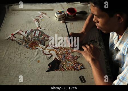 L'artigiano colora un burattino wayang kulit di Re Kresna (Krishna) nel negozio di artigianato Balai Agung a Surakarta, Giava Centrale, Indonesia. Il tradizionale teatro delle ombre dei burattini conosciuto come wayang kulit è diffuso sulle isole di Giava e Bali in Indonesia. I burattini per wayang kulit sono realizzati in pelle di bufalo. La produzione di un burattino richiede circa sei giorni. Ogni personaggio ha le proprie caratteristiche e può essere facilmente identificato dagli spettatori. Foto Stock