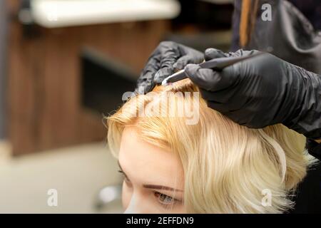 Una testa closeup di una giovane bionda che riceve tintura capelli in un salone di parrucchiere Foto Stock