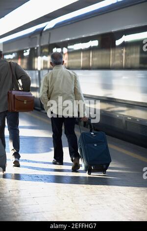 Vista posteriore di due uomini che camminano in una stazione ferroviaria, Roma, Italia Foto Stock