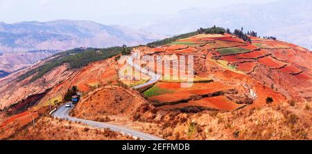 Scenario strada di montagna con colorati campi terrazzati in primavera, due auto che guidano sulla strada di montagna di Red Land, scena rurale a Dongchuan, Cina. Foto Stock