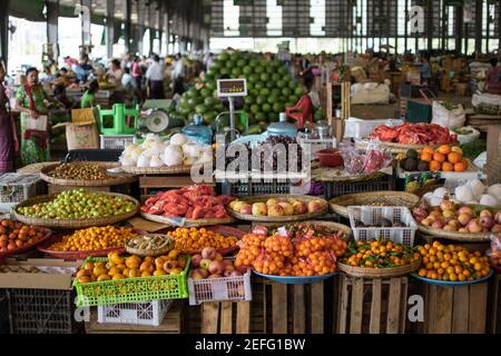 YANGON, MYANMAR - DICEMBRE 31 2019: Frutta fresca e verdura in mostra in un mercato di strada locale con i visitatori di tutti i giorni in background Foto Stock