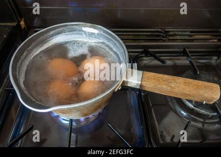Uova cucinando in una padella di acqua bollente su un piano cottura a gas. Foto Stock