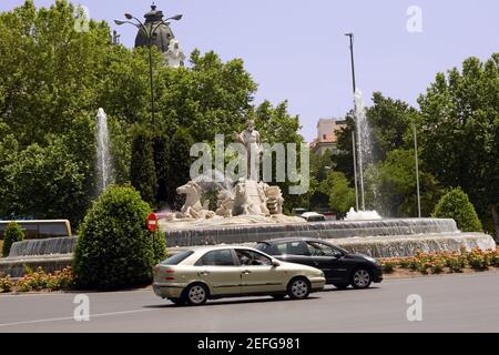 Auto che si muovono su una strada di fronte a una fontana, Fontana di Nettuno, Madrid, Spagna Foto Stock