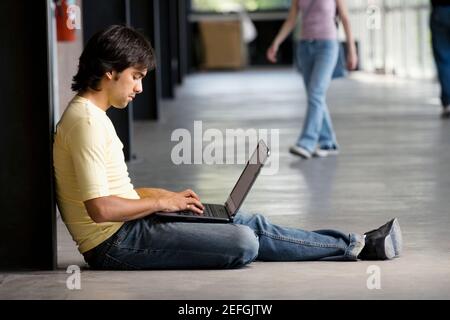 Profilo laterale di un giovane uomo che utilizza un laptop in un corridoio Foto Stock
