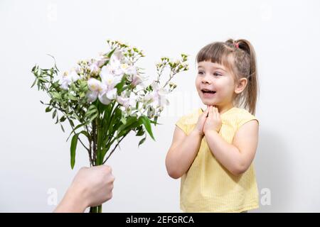 la mano di un uomo tiene fuori un bouquet di fiori bianchi ad una bambina carina in una blusa gialla Foto Stock