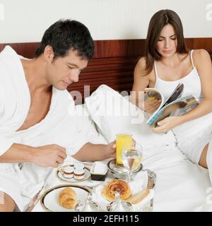 Uomo medio adulto che fa colazione con una giovane donna che legge una rivista Foto Stock