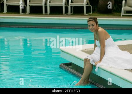 Ritratto di una sposa seduta a bordo piscina con lei piedi in acqua Foto Stock