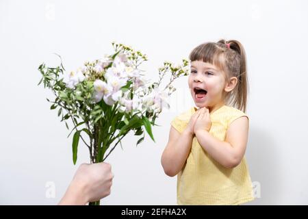 la mano di un uomo tiene fuori un mazzo di fiori bianchi ad una bambina carina in una blusa gialla. il bambino è felice Foto Stock