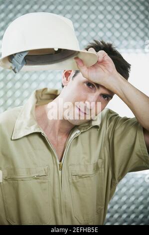 Ritratto di un uomo medio adulto che tiene un hardhat e. strofinando la fronte Foto Stock