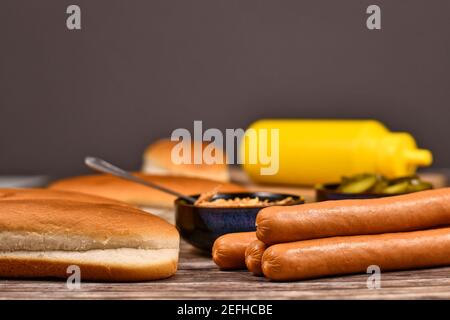 Ingredienti per fare hot dog fatti in casa con salsicce e panini in primo piano e cipolle secche, prickles e senape in background sfocato Foto Stock