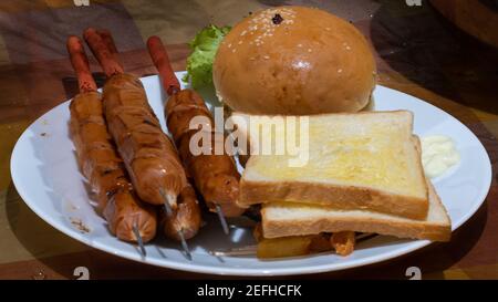 Cheeseburger con salsicce e pane affettato con burro su un piatto, deliziosa cena appetitosa è pronta a mangiare. Foto Stock