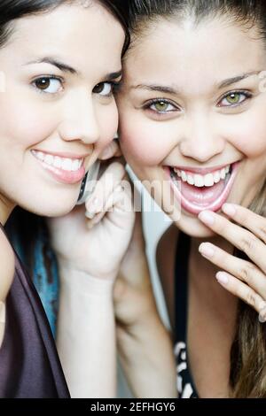 Ritratto di due giovani donne che ascoltano un telefono cellulare e sorridendo Foto Stock