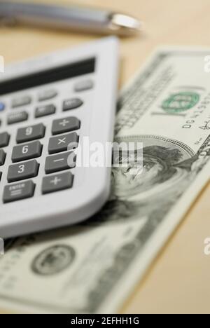 Primo piano di una calcolatrice e di un conto di cento dollari il tavolo Foto Stock