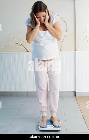 Giovane donna incinta in piedi su una bilancia Foto Stock