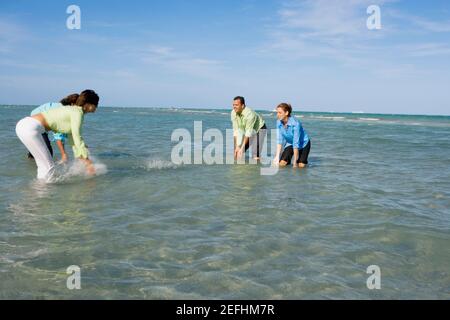 Profilo laterale di due coppie mid adult che spruzzi d'acqua sulla spiaggia Foto Stock