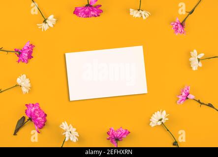 Cartoncino e mockup in carta bianca con cornice in fiori rosa e bianchi, composizione floreale con spazio per la copia, sfondo giallo Foto Stock