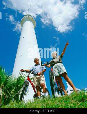 Vista ad angolo basso di una coppia anziana che si trova di fronte ad una torre con le loro biciclette, Bermuda Foto Stock