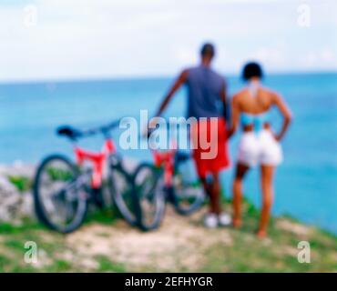 Vista posteriore di una giovane coppia in piedi con biciclette sulla costa, Bermuda Foto Stock