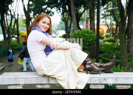 Ritratto di una giovane donna seduta su una balaustra dentro un parco Foto Stock