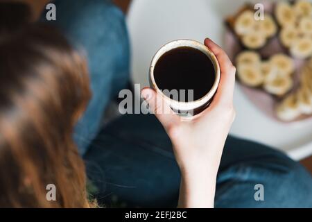 Donna tiene una tazza di caffè nero, colpo candida. Dopo la colazione, bere il caffè del mattino a casa Foto Stock