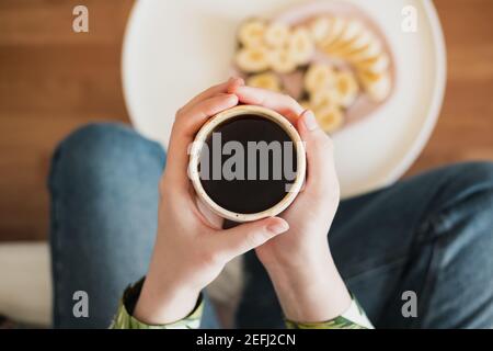 Donna tiene una tazza di caffè nero, sparato direttamente sopra. Dopo la colazione, bere il caffè del mattino a casa Foto Stock