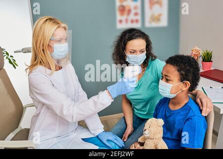 Medico generico che usa il termometro infrarosso misura la temperatura corporea del ragazzo durante un coronavirus pandemico Foto Stock