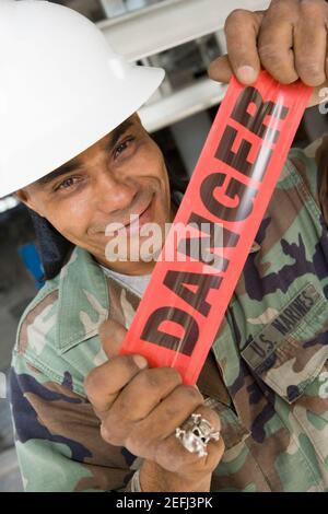 Ritratto di un operaio di costruzione maschio che tiene un nastro di cordone e smirando Foto Stock