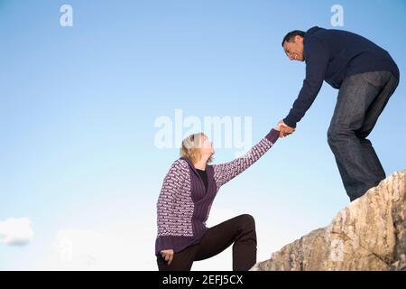 Uomo maturo che aiuta una donna matura a salire su una roccia Foto Stock