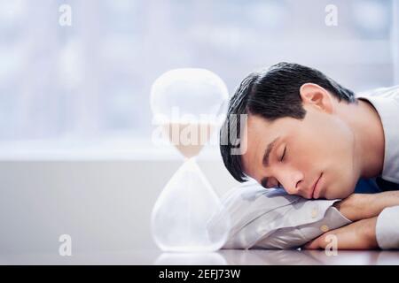 Primo piano di un uomo d'affari che dormiva di fronte a una clessidra Foto Stock