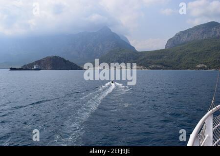 Nave da carico che naviga lungo la costa contro il cielo blu nuvoloso e mare increspato vicino all'isola delle tartarughe, Antalia, Turchia. Foto Stock
