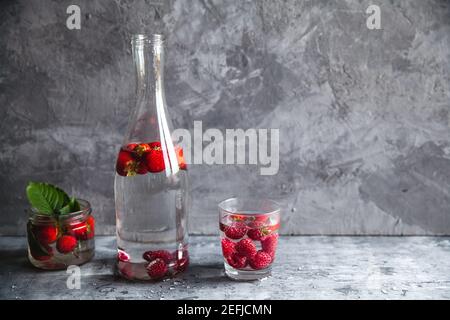 Fragole in acqua su sfondo grigio scuro. Cibo sano, frutta. Un bouquet di fiori come decorazione Foto Stock