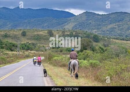 Gaucho argentino a cavallo e due ciclisti che percorrono la strada nazionale 9 / Ruta Nacional 9, sezione Salta-Jujuy nell'Argentina settentrionale Foto Stock