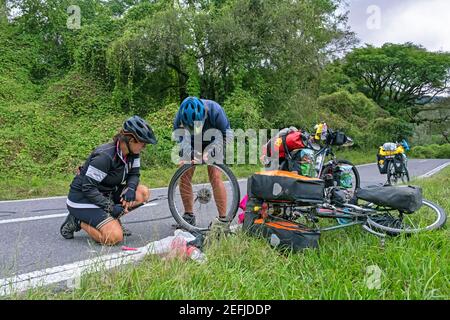 Due ciclisti femminili che riparano pneumatici per biciclette in piano lungo la National Route 9 / Ruta Nacional 9, sezione Salta-Jujuy nell'Argentina settentrionale Foto Stock