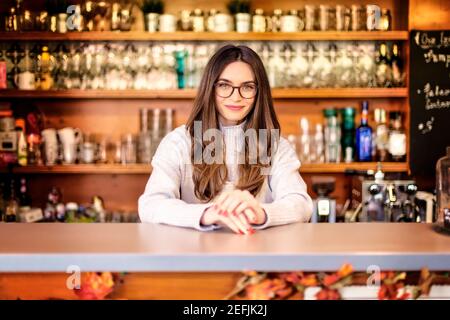 Un'allegra e sorridente cameriera che si trova dietro il bancone del bar mentre attende gli ospiti. Piccola impresa. Foto Stock