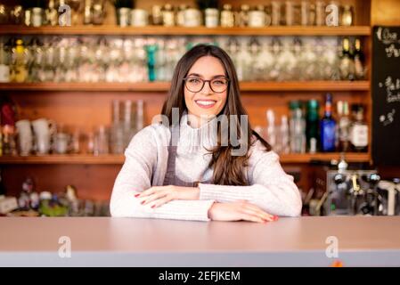 Un'allegra e sorridente cameriera che si trova dietro il bancone del bar mentre attende gli ospiti. Piccola impresa. Foto Stock