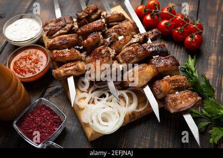 Costolette di agnello grigliate su un tagliere con spezie e salsa. Vista dall'alto su un tavolo di legno scuro Foto Stock