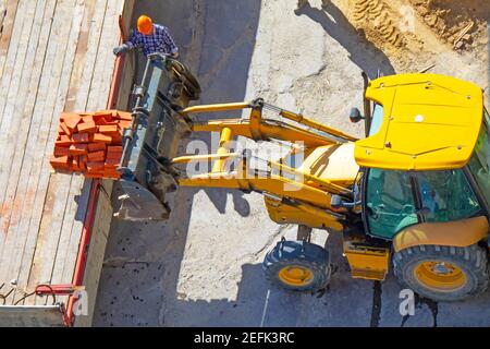 Caricamento di mattoni nel cassone di carico di un carrello mediante un trattore con benna Foto Stock